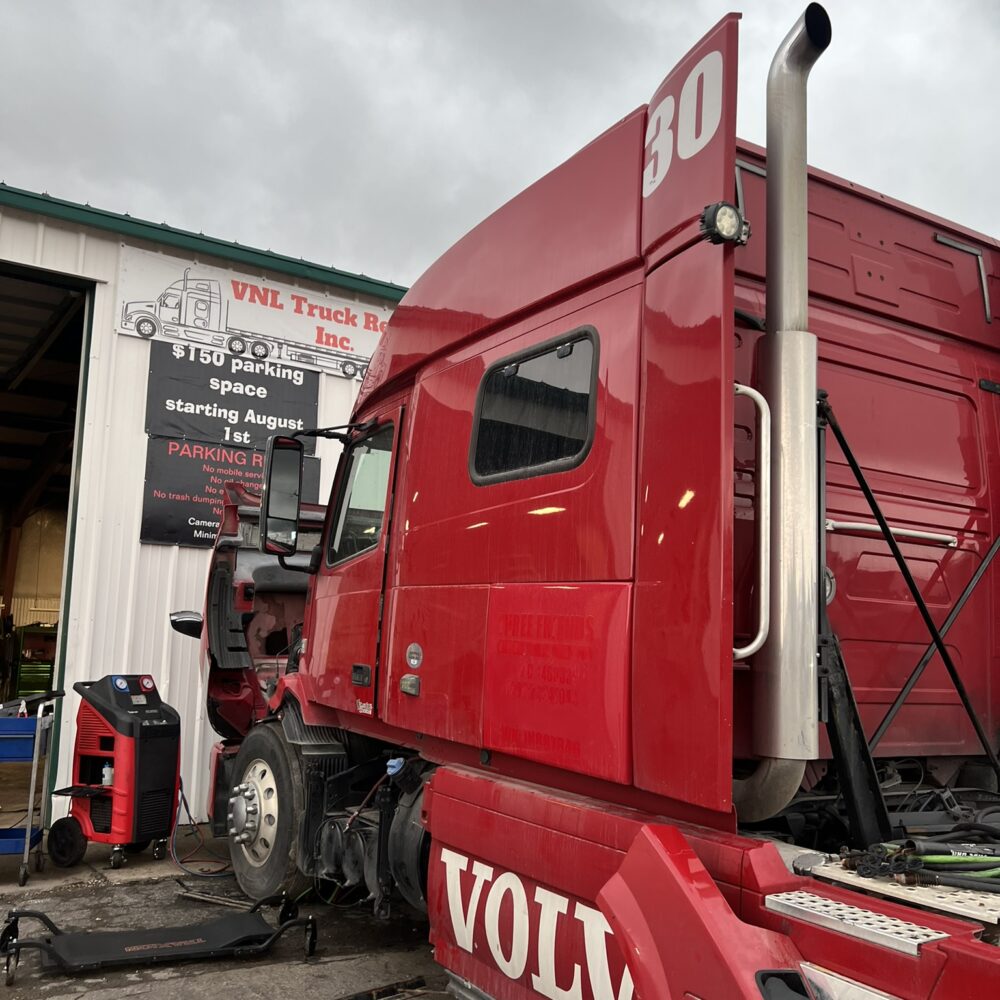 A red Volvo semi truck with the door open, undergoing preparation for the cabin to be removed.