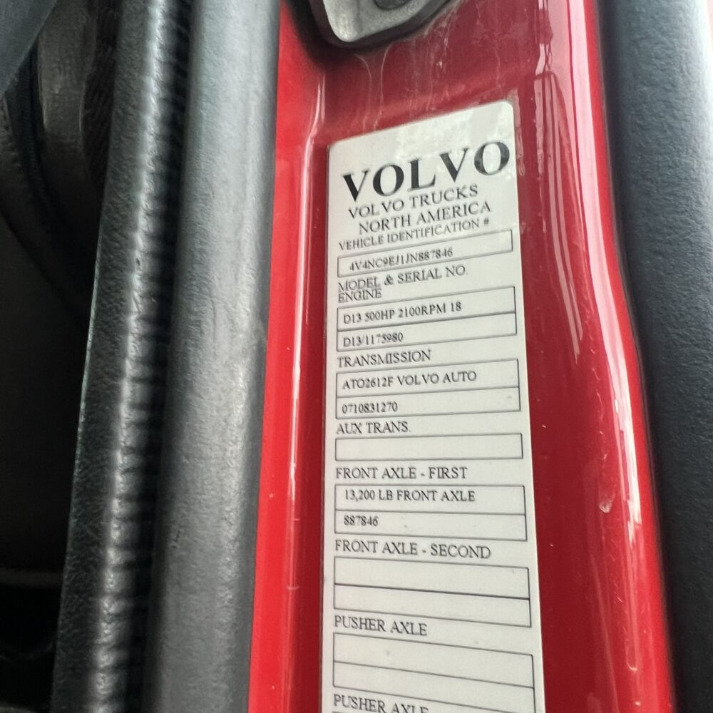 Close-up of the vehicle identification tag on a red Volvo semi truck, displaying model, serial number, engine information, and axle details.