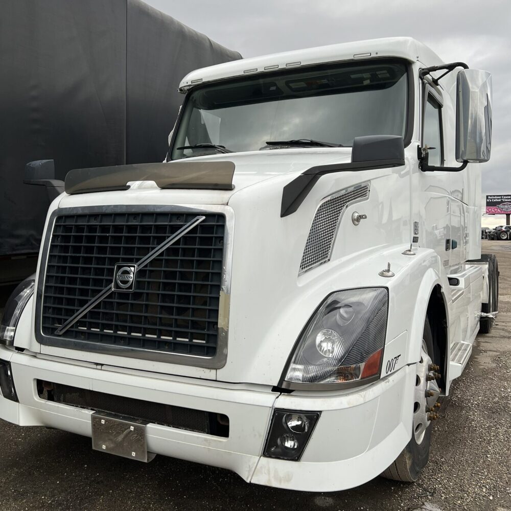 White Volvo semi truck front view parked on gravel lot.